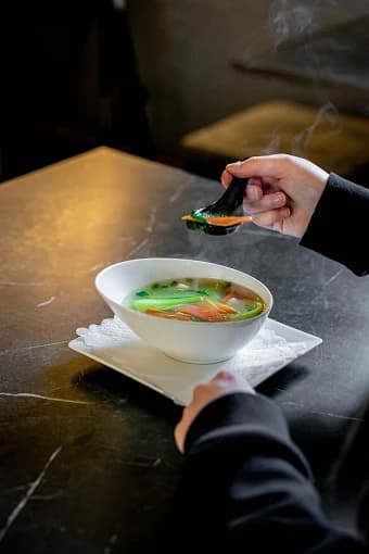 Klare Suppe mit Gemüsestreifen in einer weißen Schale
