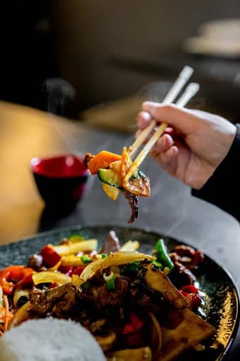 Wok-Gericht wird mit Stäbchen gehalten