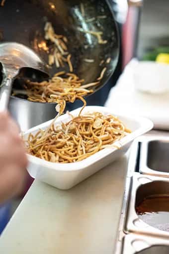 Gebratene Nudeln kommen aus dem Wok in die Lieferbox